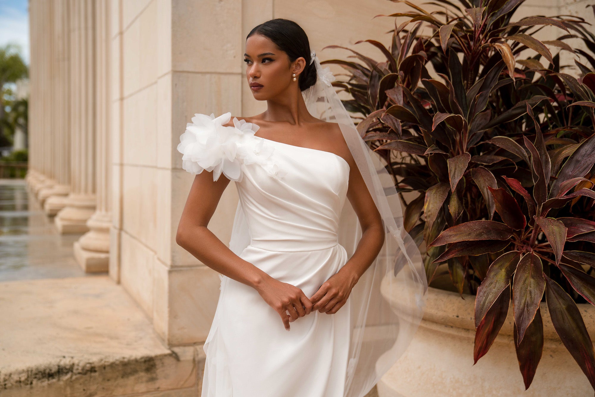 Close-up of a white wedding dress with a ruched bodice and layered 3D floral shoulder detail