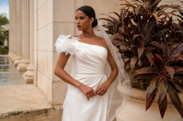 Close-up of a white wedding dress with a ruched bodice and layered 3D floral shoulder detail