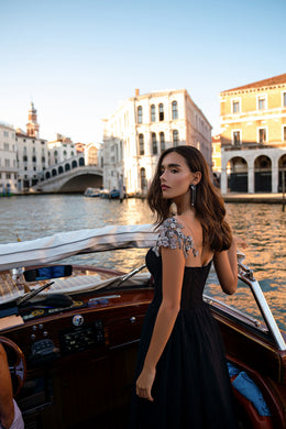 Black evening dress featuring a fitted bodice, sheer shoulder accents, and a full flowing skirt