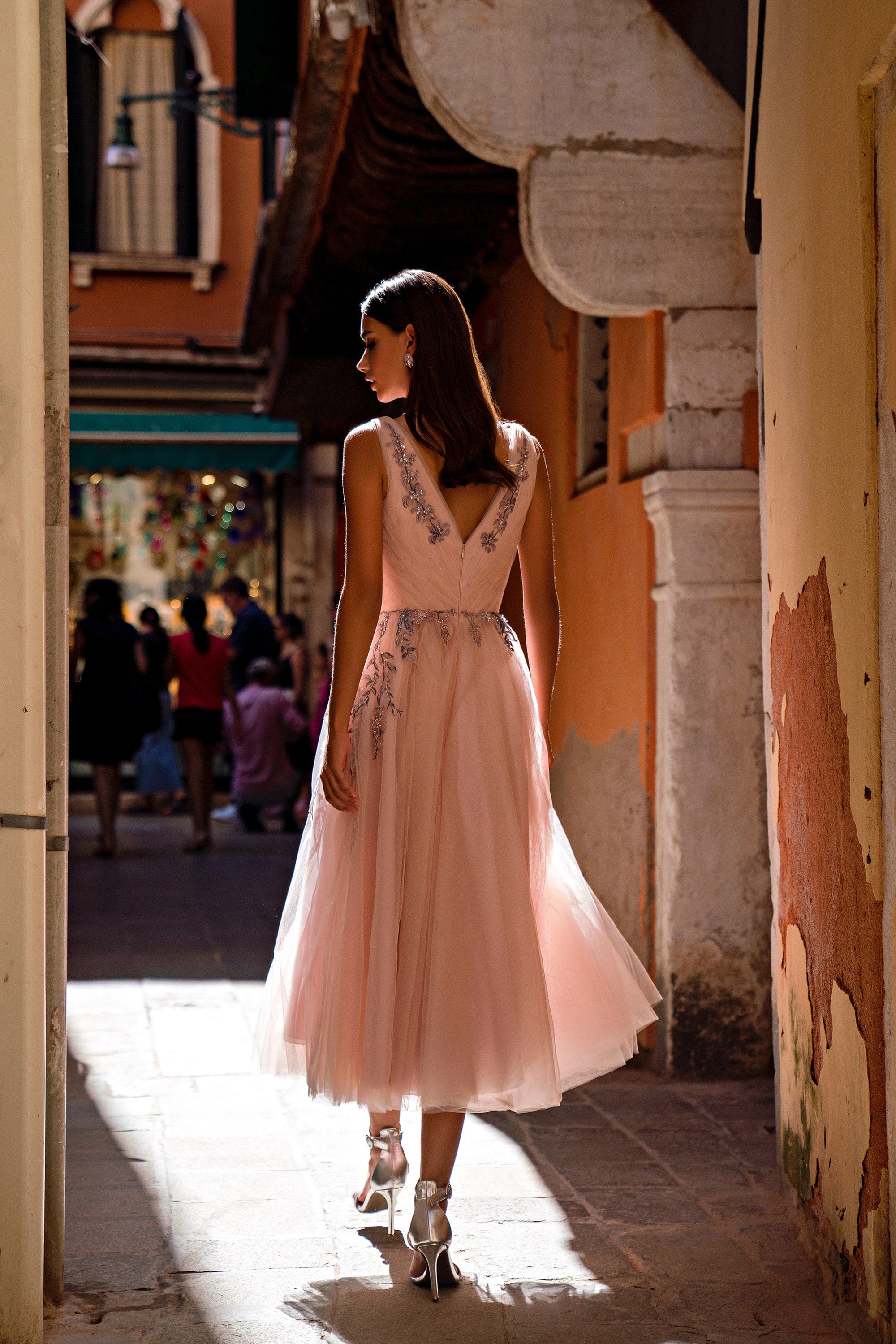 Back of a blush pink evening dress with a V-shaped back, embellished waist, and flowing tulle skirt