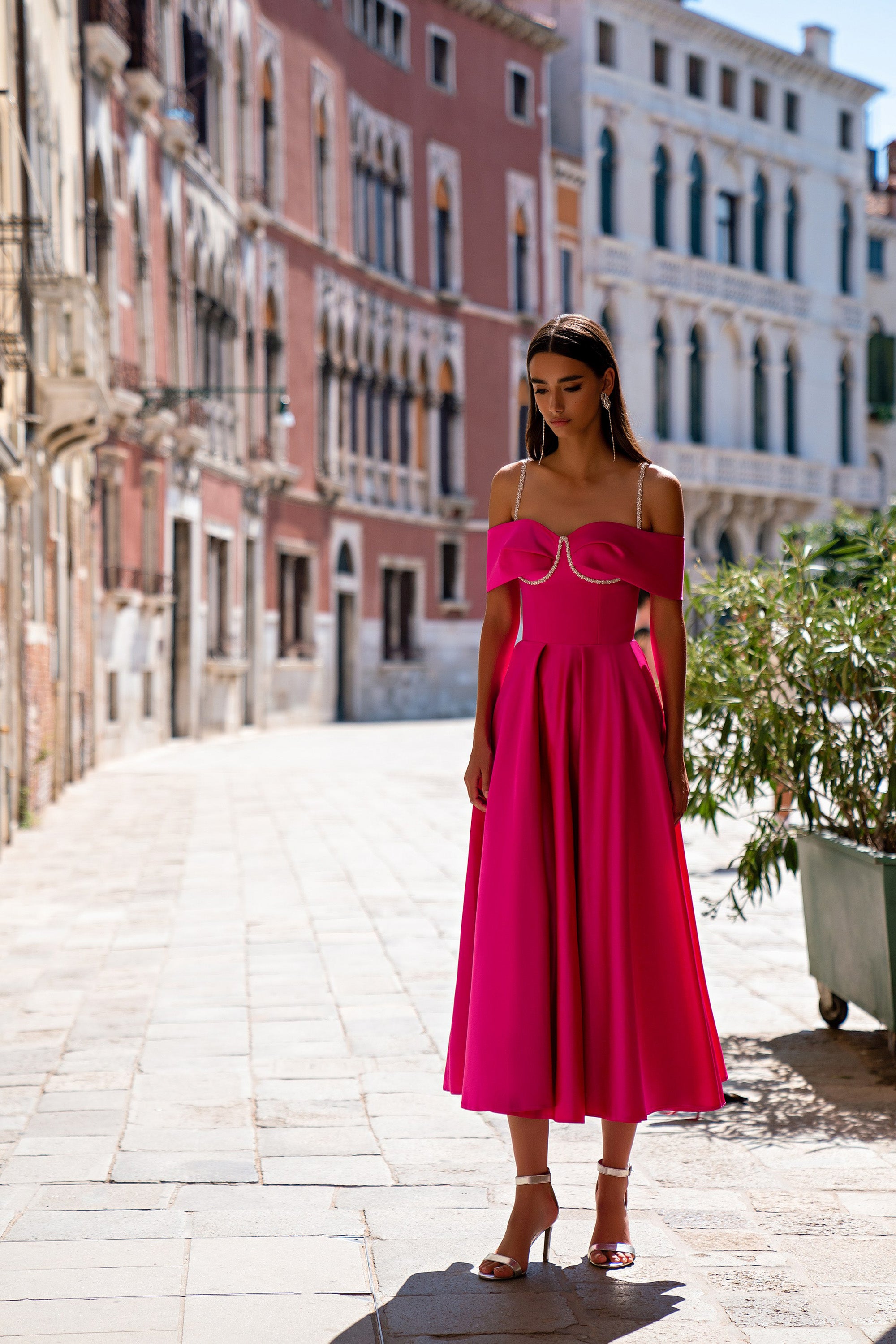 Fuchsia evening dress with draped off-the-shoulder sleeves, delicate straps, and a flowing pleated midi-length skirt