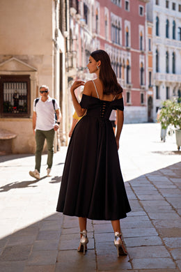 Black evening dress showing a corset-style lace-up back, off-the-shoulder sleeves, thin straps, and a full pleated skirt