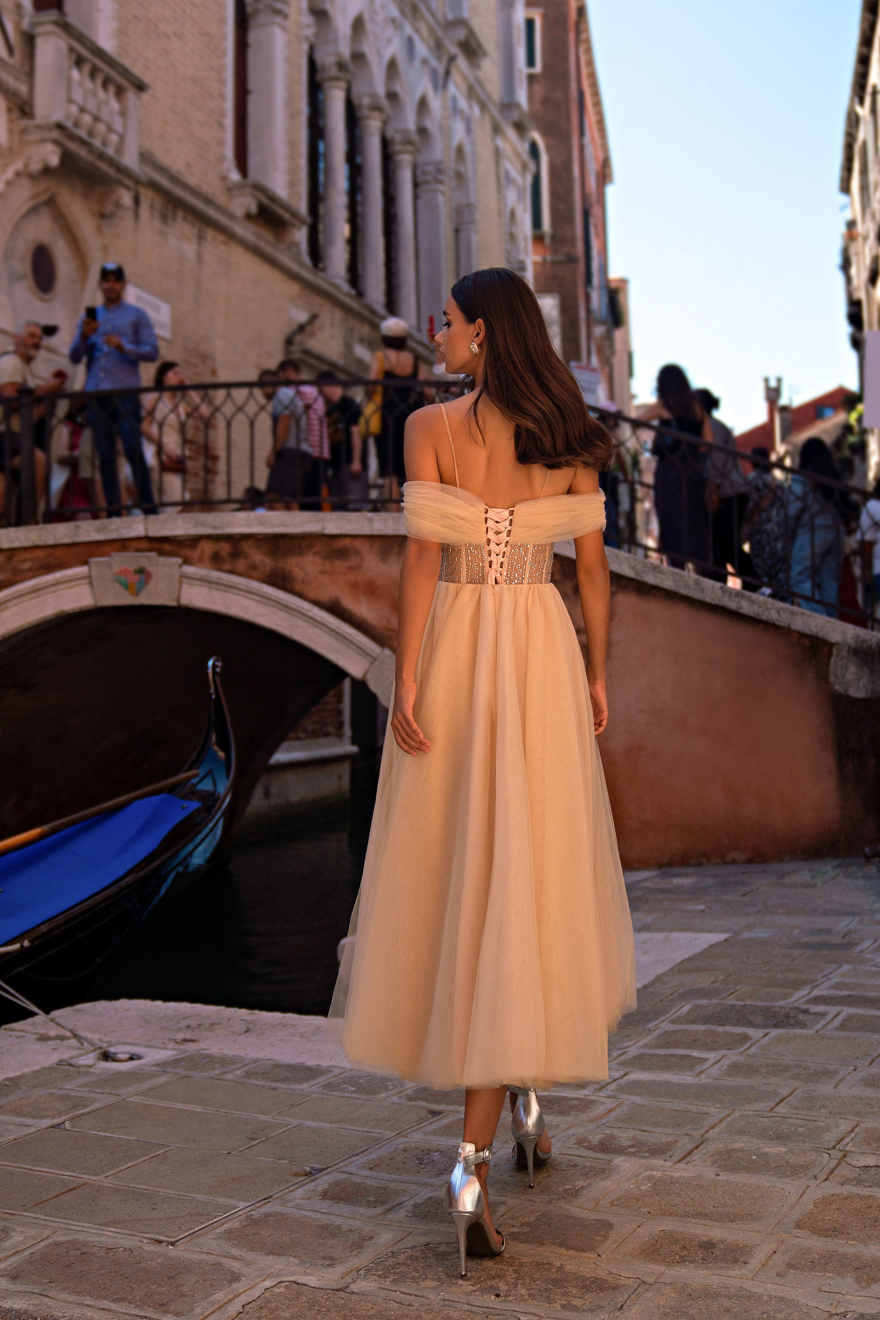 Back view of a champagne evening dress showing corset-style lacing, off-shoulder tulle, and a flowing skirt