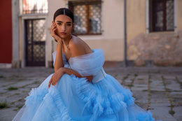Light blue evening dress featuring voluminous sheer sleeves and cascading ruffles across the full skirt