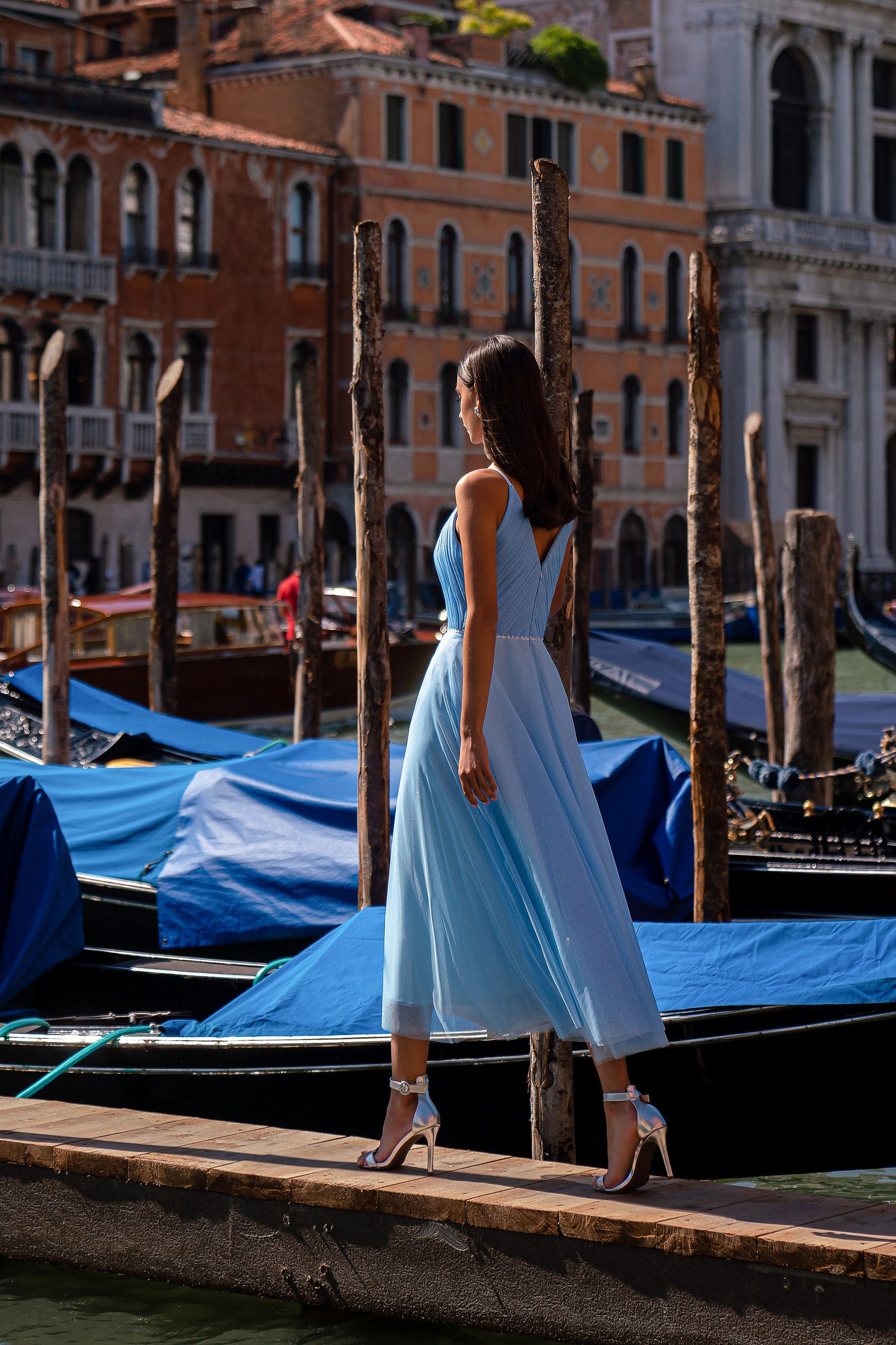 Blue sleeveless evening dress with a low V-back, fitted waist, and shimmering tea-length skirt