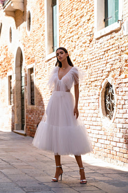 White tiered evening dress featuring a deep V-neckline, sheer flutter sleeves, and a full pleated skirt
