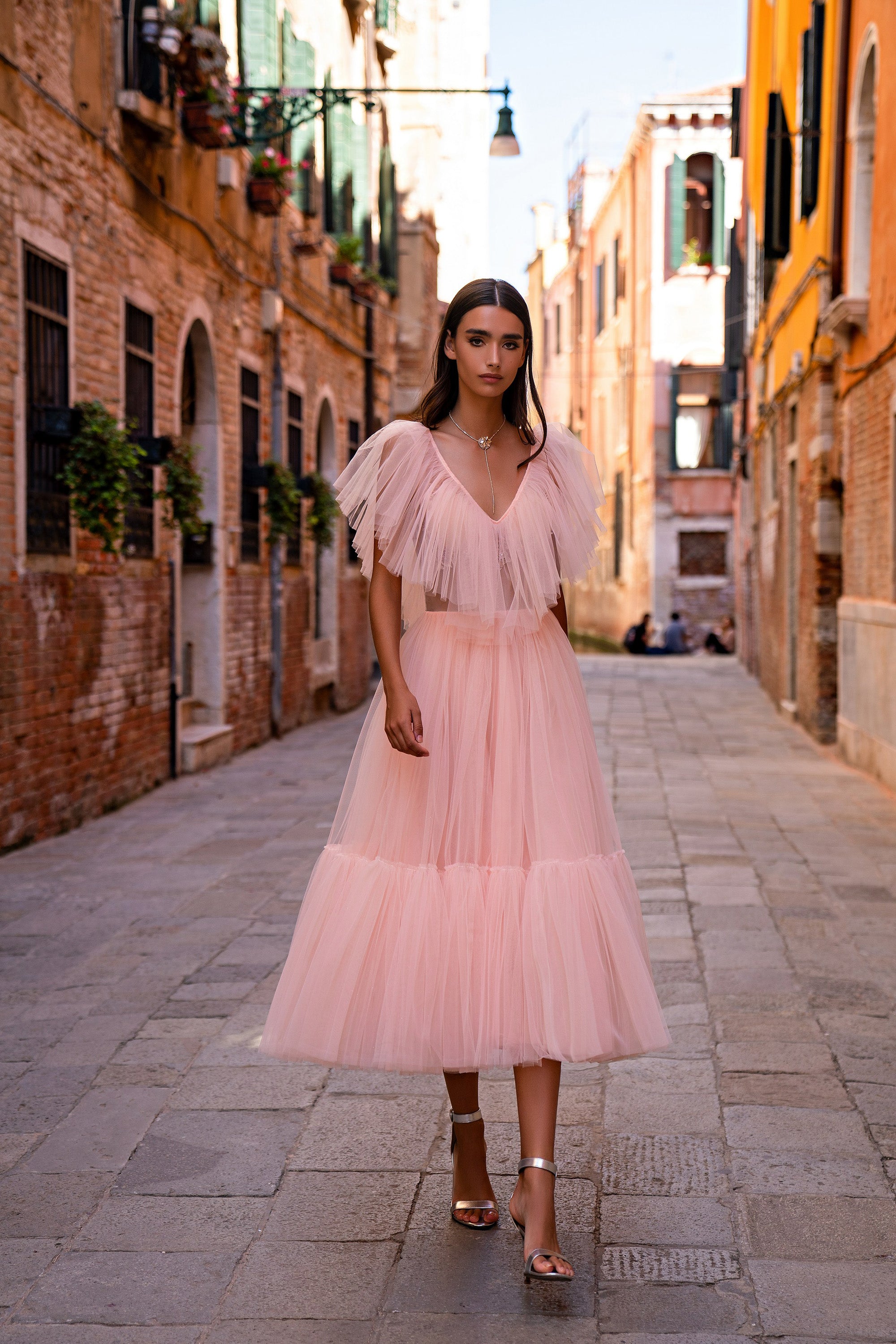 Pink evening dress with a deep V-neckline, layered sheer flutter sleeves, and a tiered pleated skirt