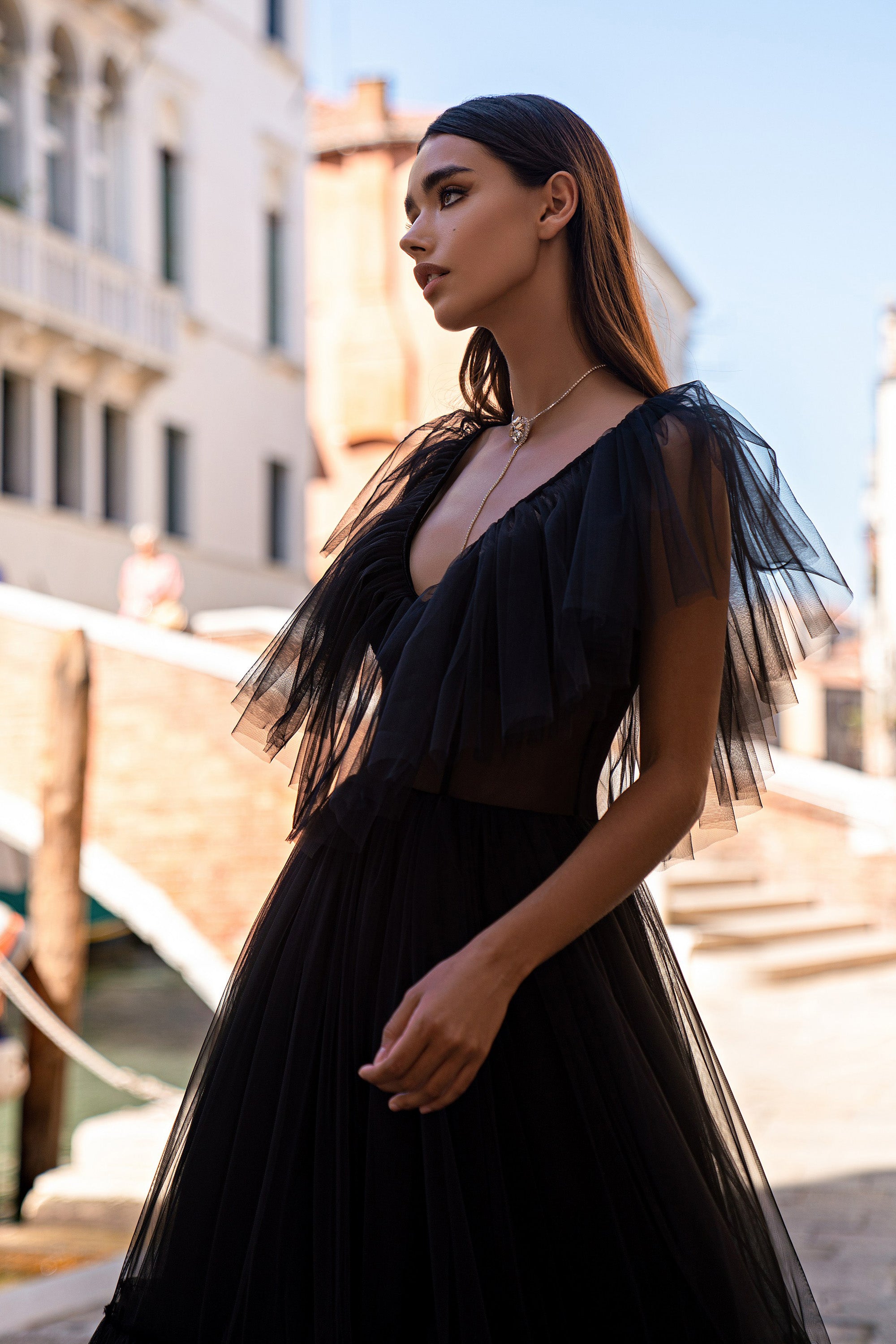 Black evening dress with a deep V-neckline, sheer fringed flutter sleeves, and a flowing pleated skirt
