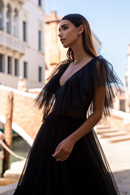 Black evening dress with a deep V-neckline, sheer fringed flutter sleeves, and a flowing pleated skirt
