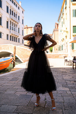 Black evening dress with a deep V-neckline, sheer layered sleeves, fitted waist, and full tiered skirt