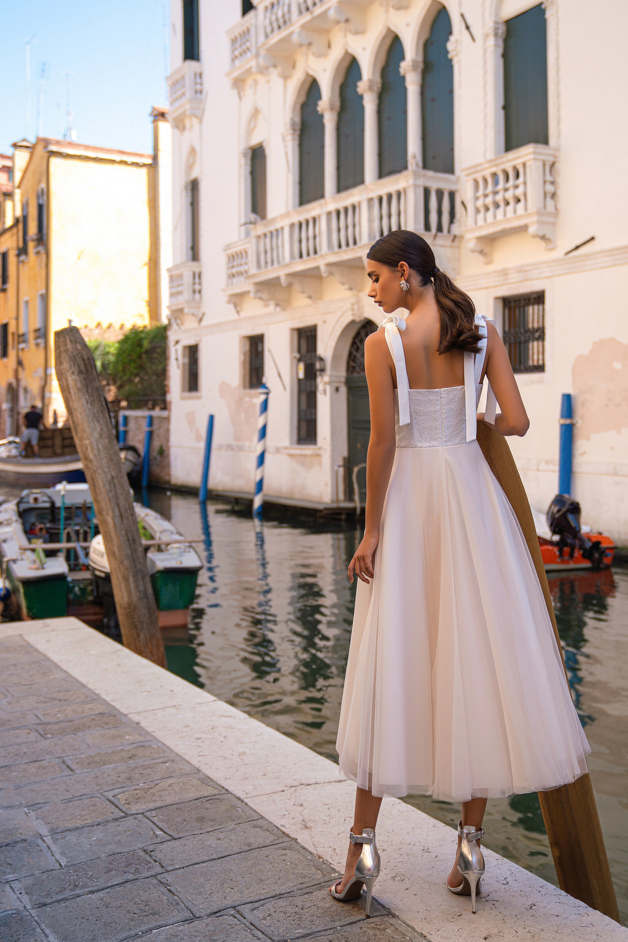 Back of an ivory evening dress showing its open upper back, embellished waist, and full flowing midi skirt