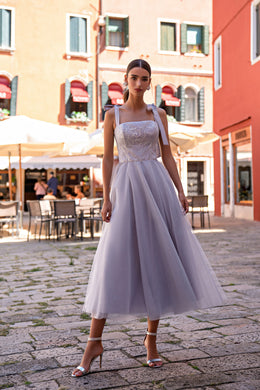 Ivory evening dress with a fitted sequin bodice, square neckline, ribbon straps, and flowing midi skirt