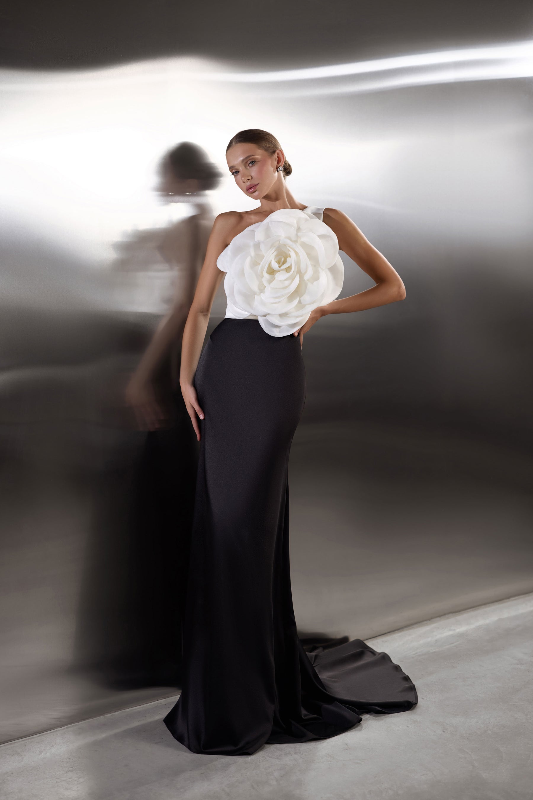 Floor-length black evening dress with an oversized white flower bodice and a dramatic pooling train