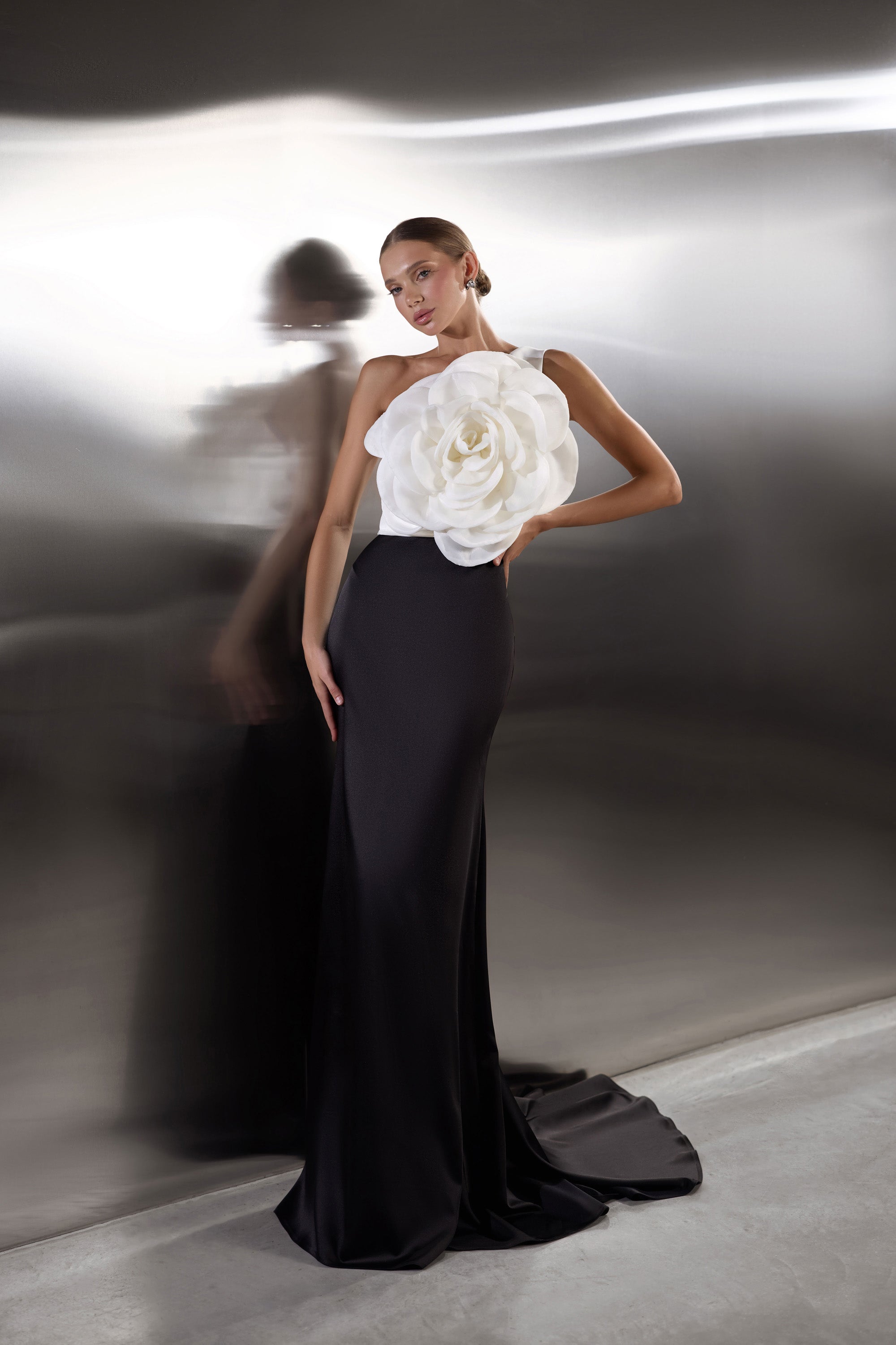 Floor-length black evening dress with an oversized white flower bodice and a dramatic pooling train