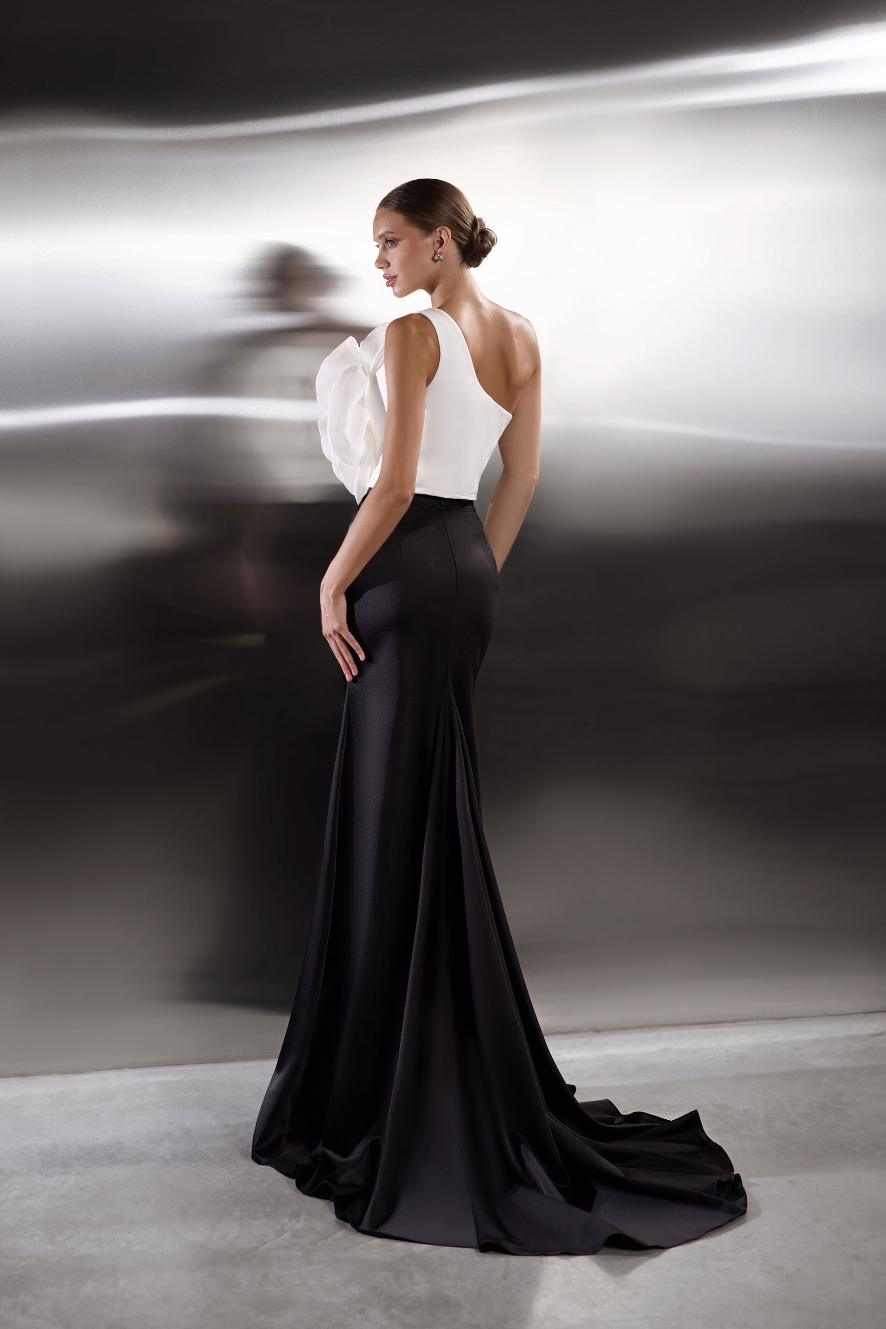 Open-back black evening dress with a white floral bodice accent, fitted skirt, and sweeping train