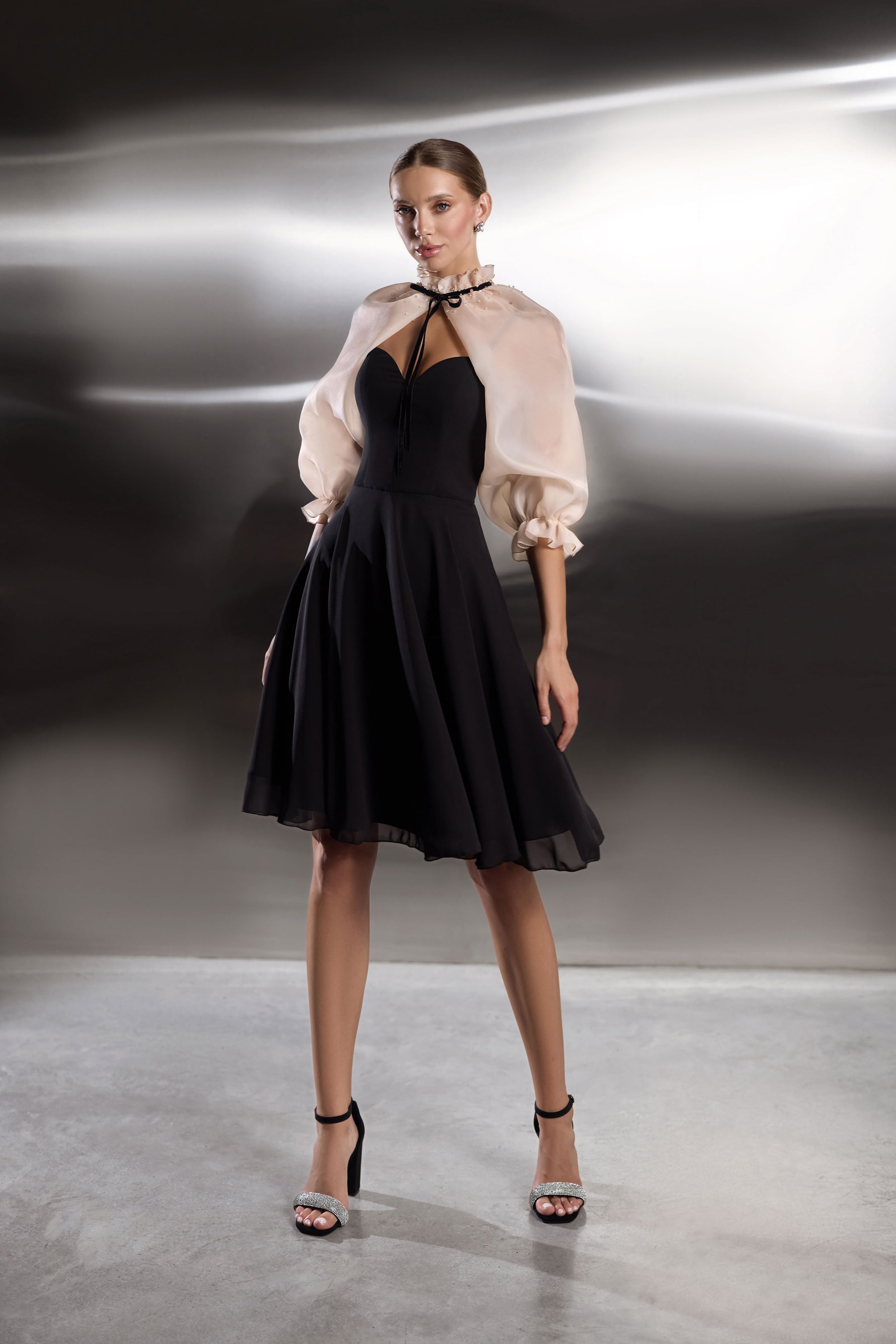Black evening dress with a full midi skirt, cutout neckline, and sheer blush puff-sleeve capelet