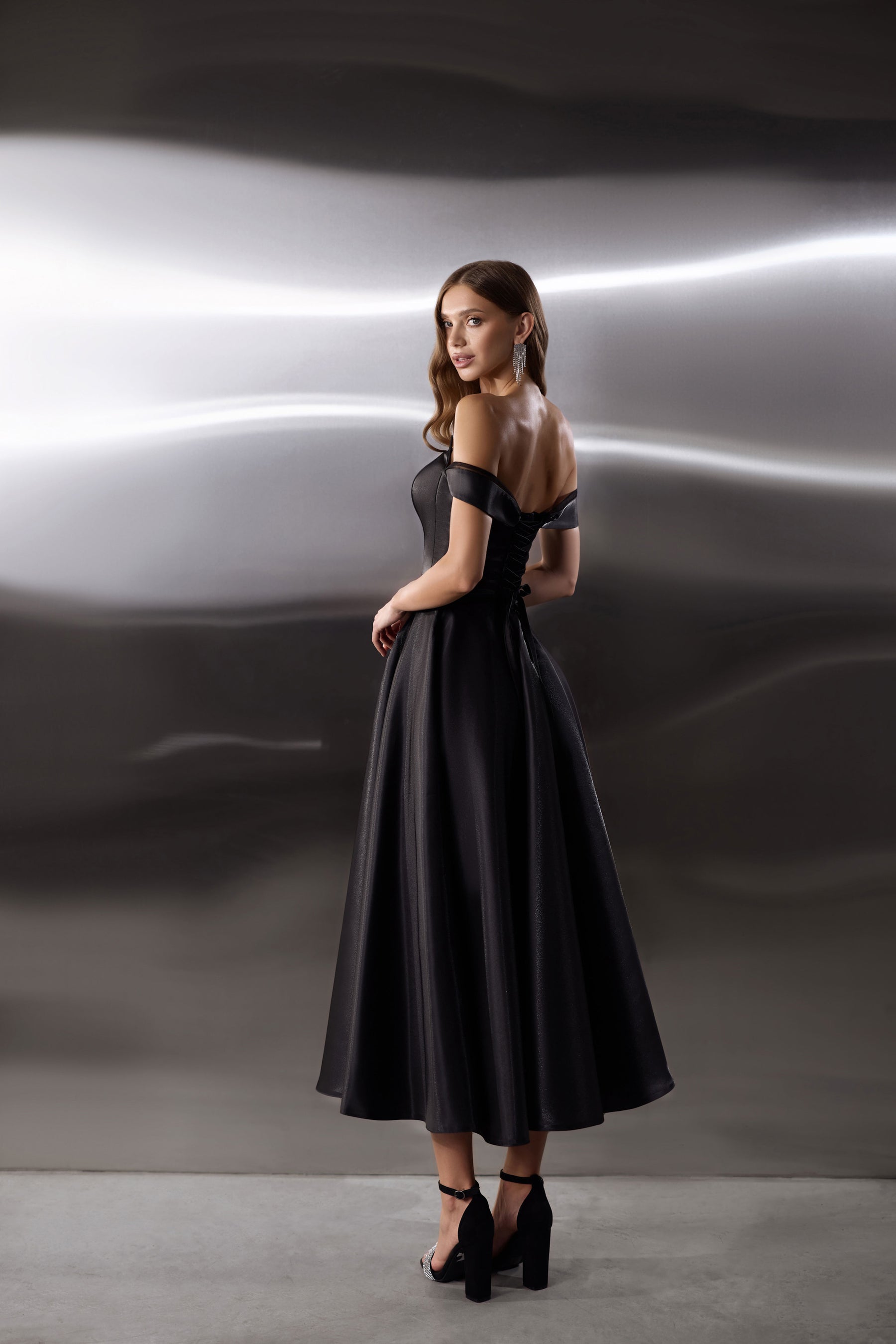 Black evening dress showing an open back, off-shoulder sleeves, fitted waist, and flowing full skirt