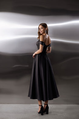 Black evening dress showing an open back, off-shoulder sleeves, fitted waist, and flowing full skirt