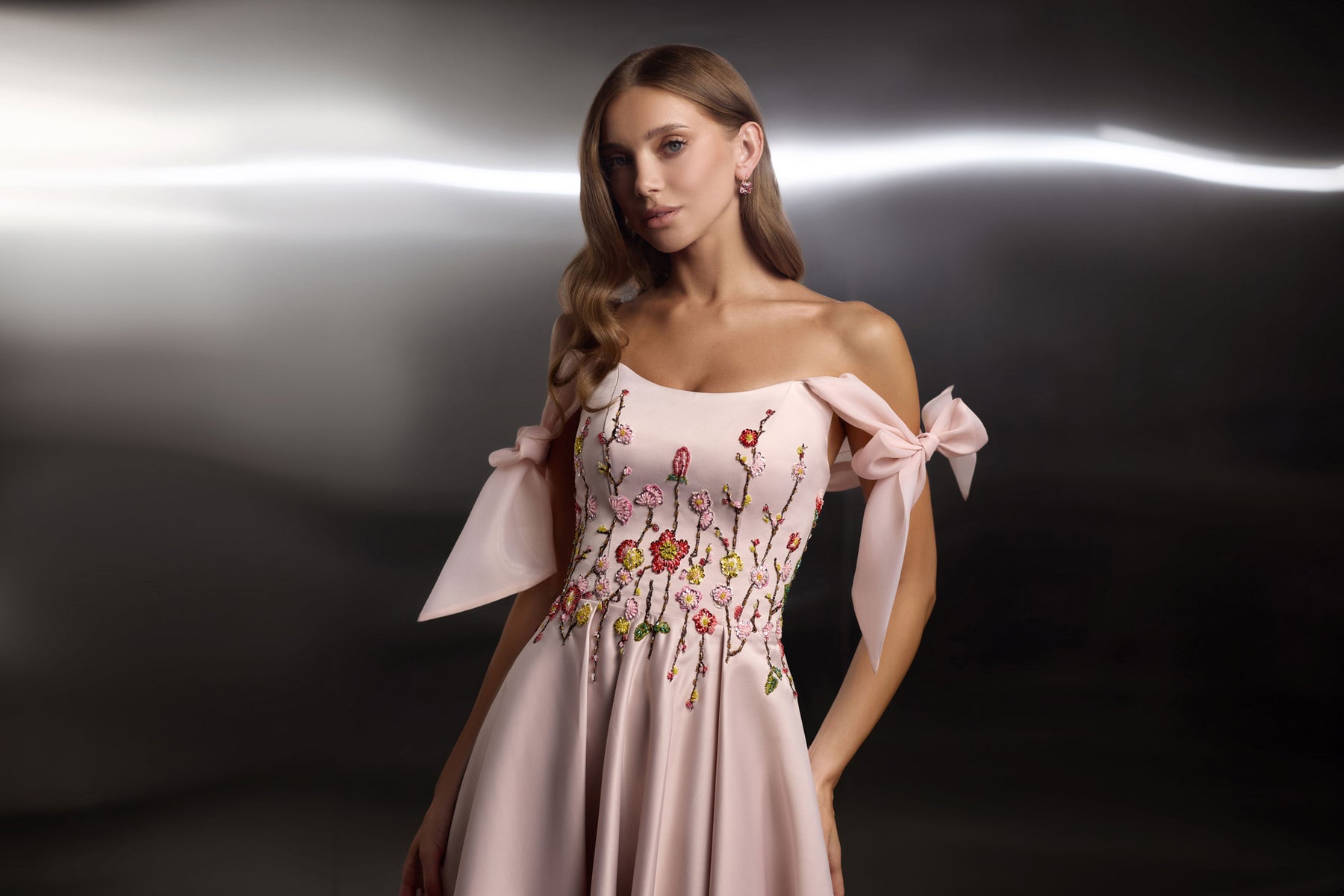 Close-up of a blush pink evening dress with colorful floral embroidery, square neckline, and off-shoulder ribbon bows