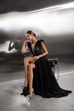 Black evening dress with a sparkling V-neck bodice, feathered cap sleeves, thigh-high slit, and long train