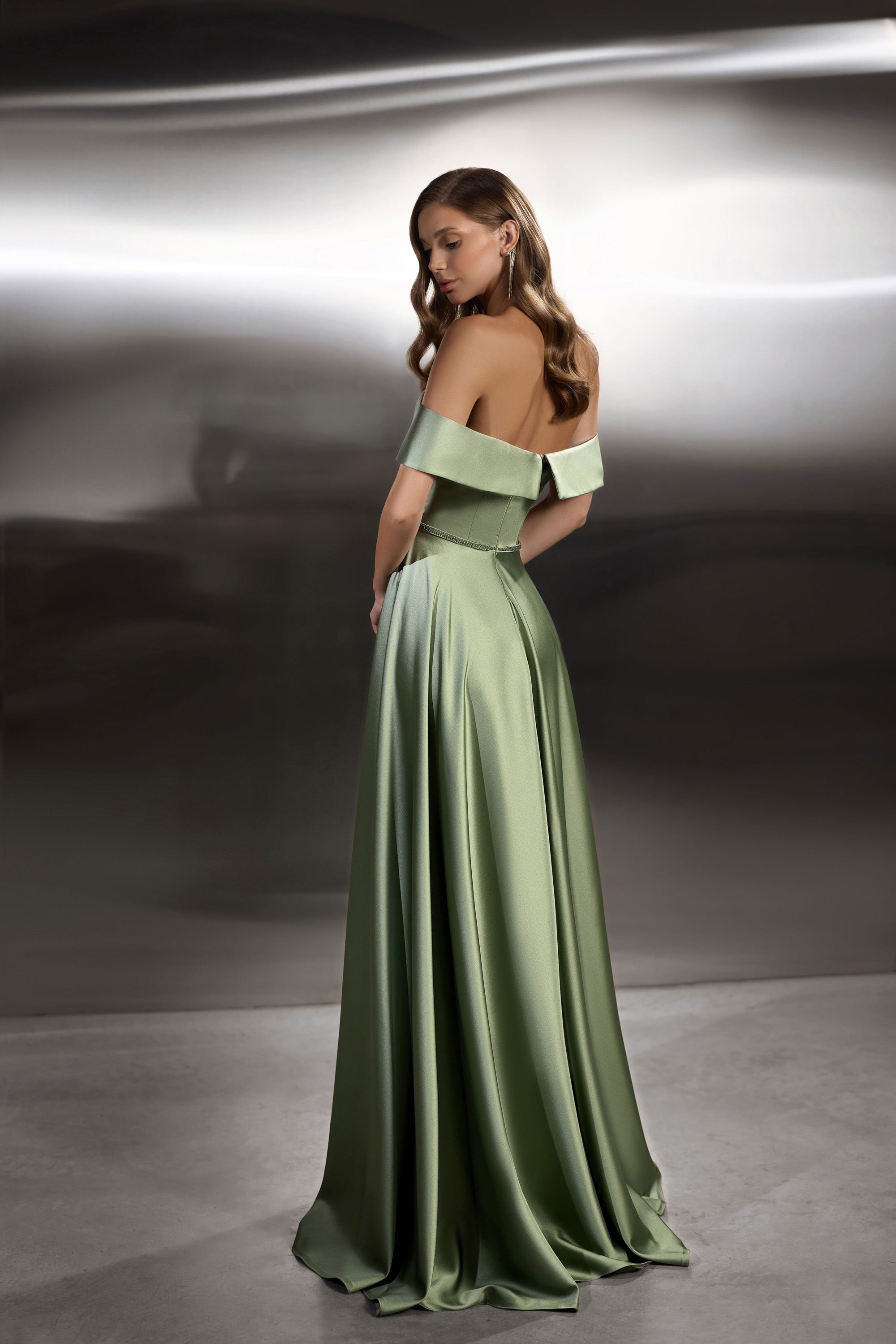 Sage green evening dress showing an open back, off-the-shoulder band, fitted waist, and long flowing skirt