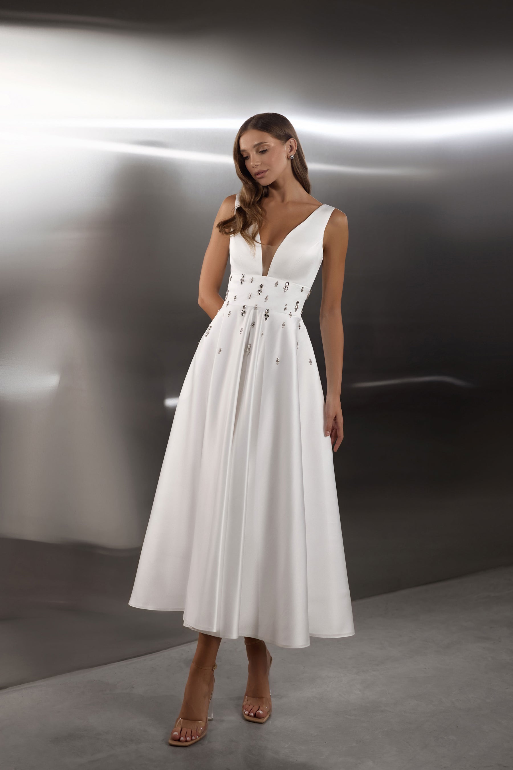 White evening dress with a deep V-neckline, sleeveless bodice, embellished waist, and flowing A-line skirt