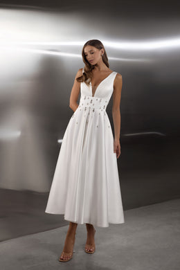 White evening dress with a deep V-neckline, sleeveless bodice, embellished waist, and flowing A-line skirt