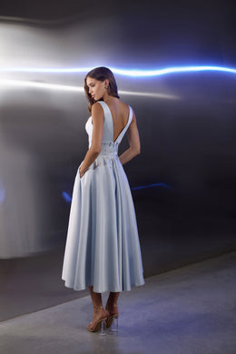 Open-back pale blue evening dress with crossing straps, jeweled waist details, and a flowing pleated skirt
