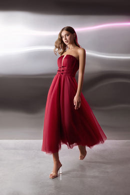 Red strapless evening dress with a ruched bodice, defined waist, and flowing sheer-overlay skirt
