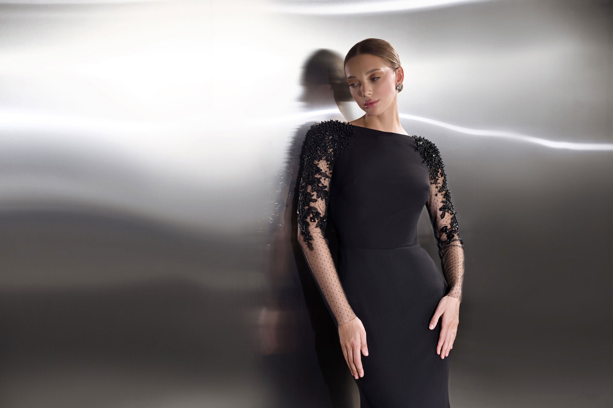 Close-up of a black evening dress with sheer floral lace sleeves and a high rounded neckline