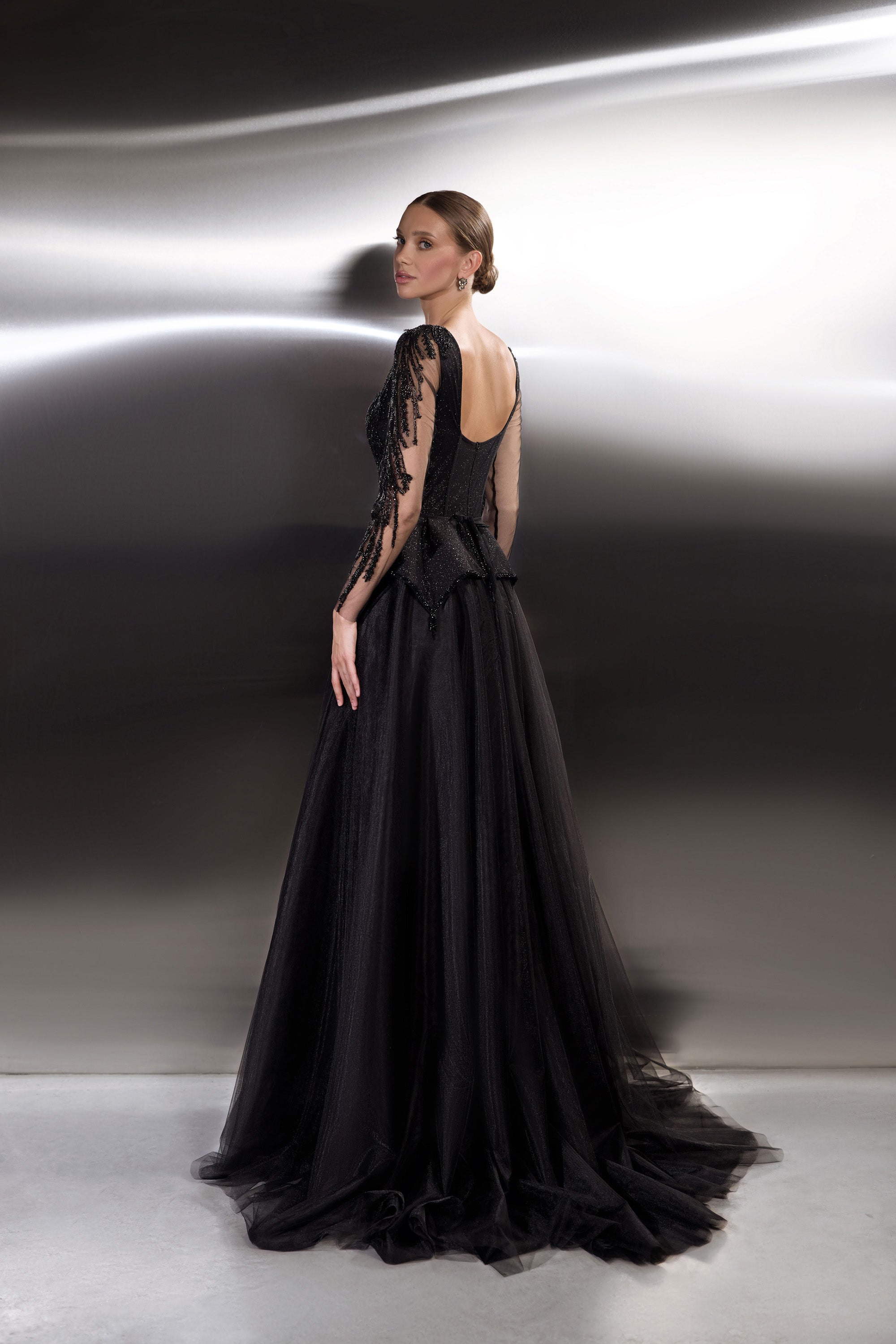 Low open back and sheer embellished sleeves on a black evening dress with a sweeping floor-length train