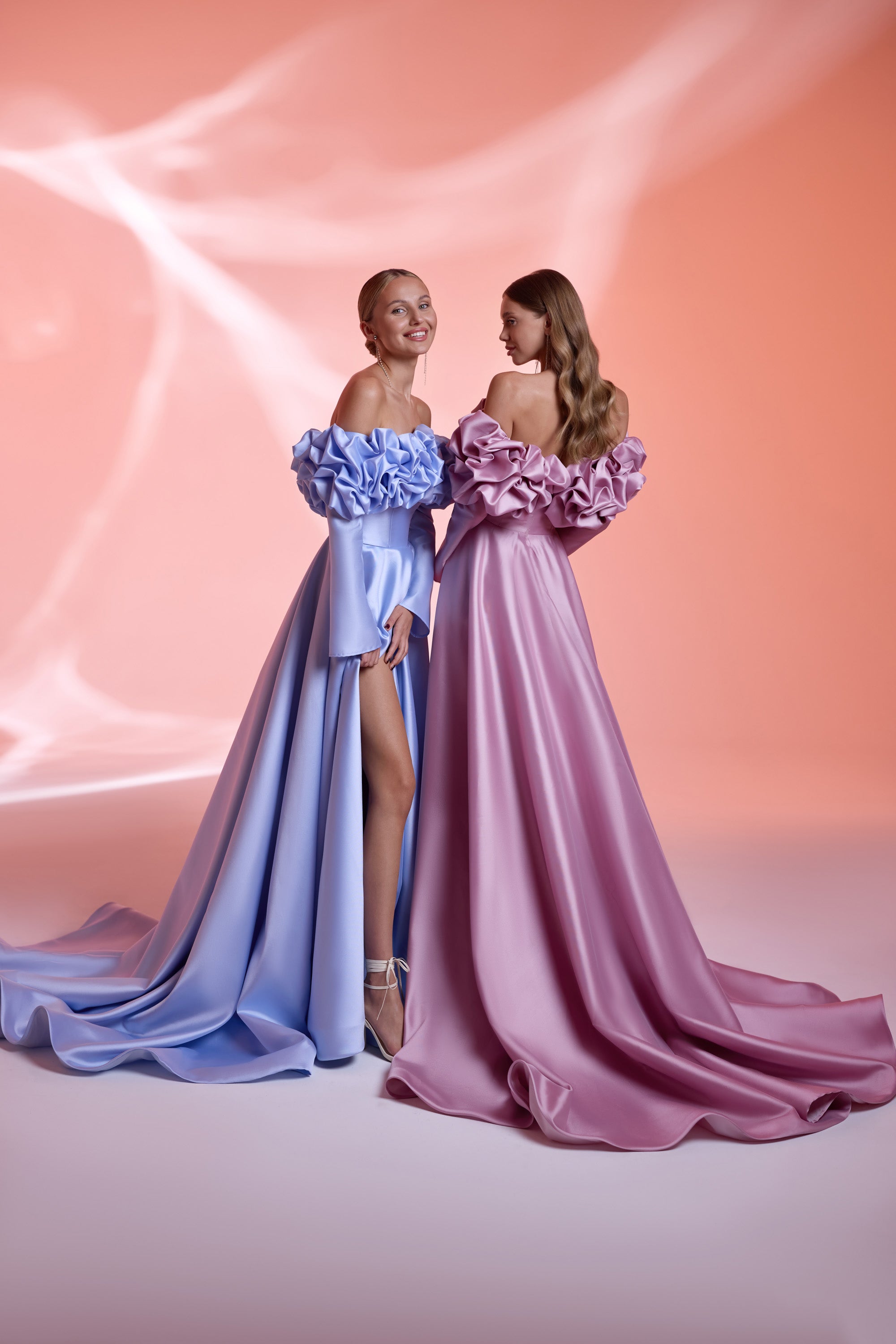 Blue and mauve satin evening dresses with off-the-shoulder ruffled bodices, long sleeves, slits, and trains