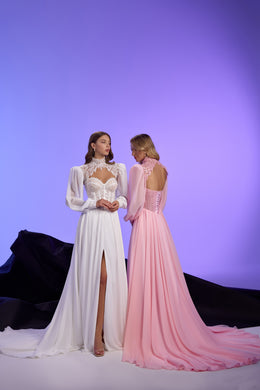 White evening dress with lace bodice, thigh-high slit, and long train beside a pink dress with an open lace-up back