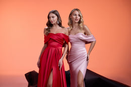 Close-up of red and blush pink evening dresses with ruched bodices, off-the-shoulder sleeves, and high slits