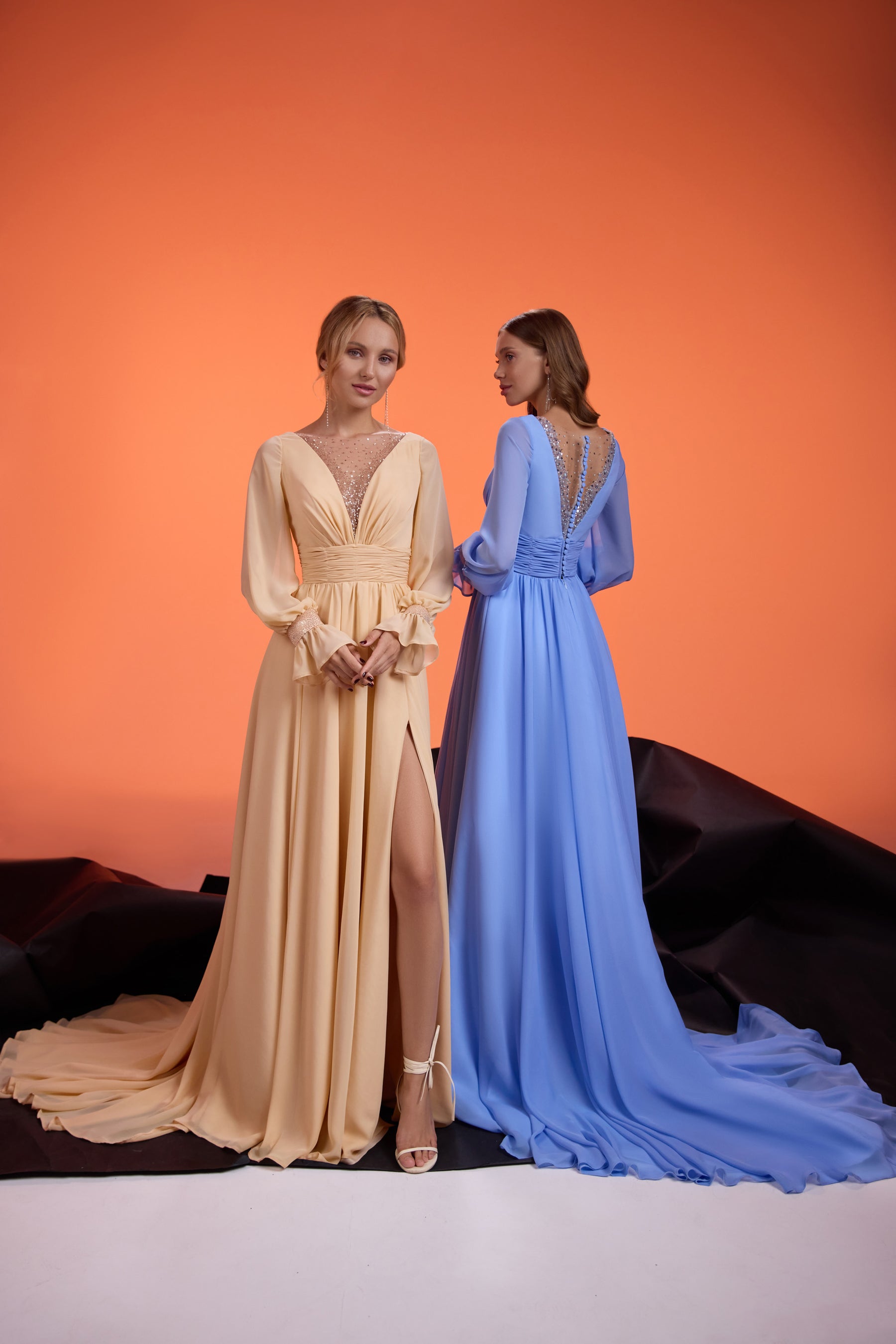 Blue evening dress with an open V-back, long sleeves, gathered waist, and sweeping floor-length train
