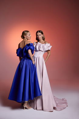 Blush pink evening dress with a ruffled off-shoulder neckline, flowing skirt, and long trailing train