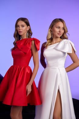 Close-up of a white evening dress with a sculptural shoulder bow, fitted waist, and high slit