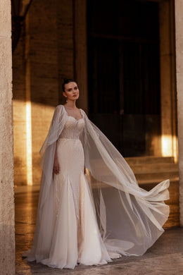 Glittering ivory wedding dress with a sweetheart neckline, fitted trumpet silhouette, and sweeping sheer cape