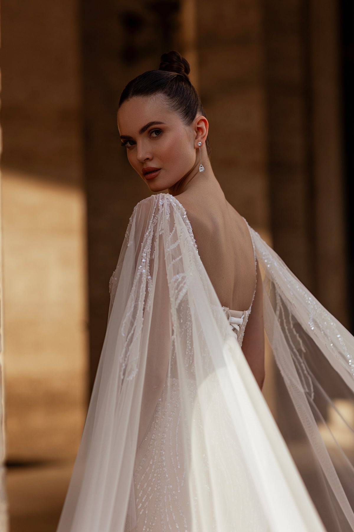 Open-back ivory wedding dress with a sheer beaded cape and low back detail