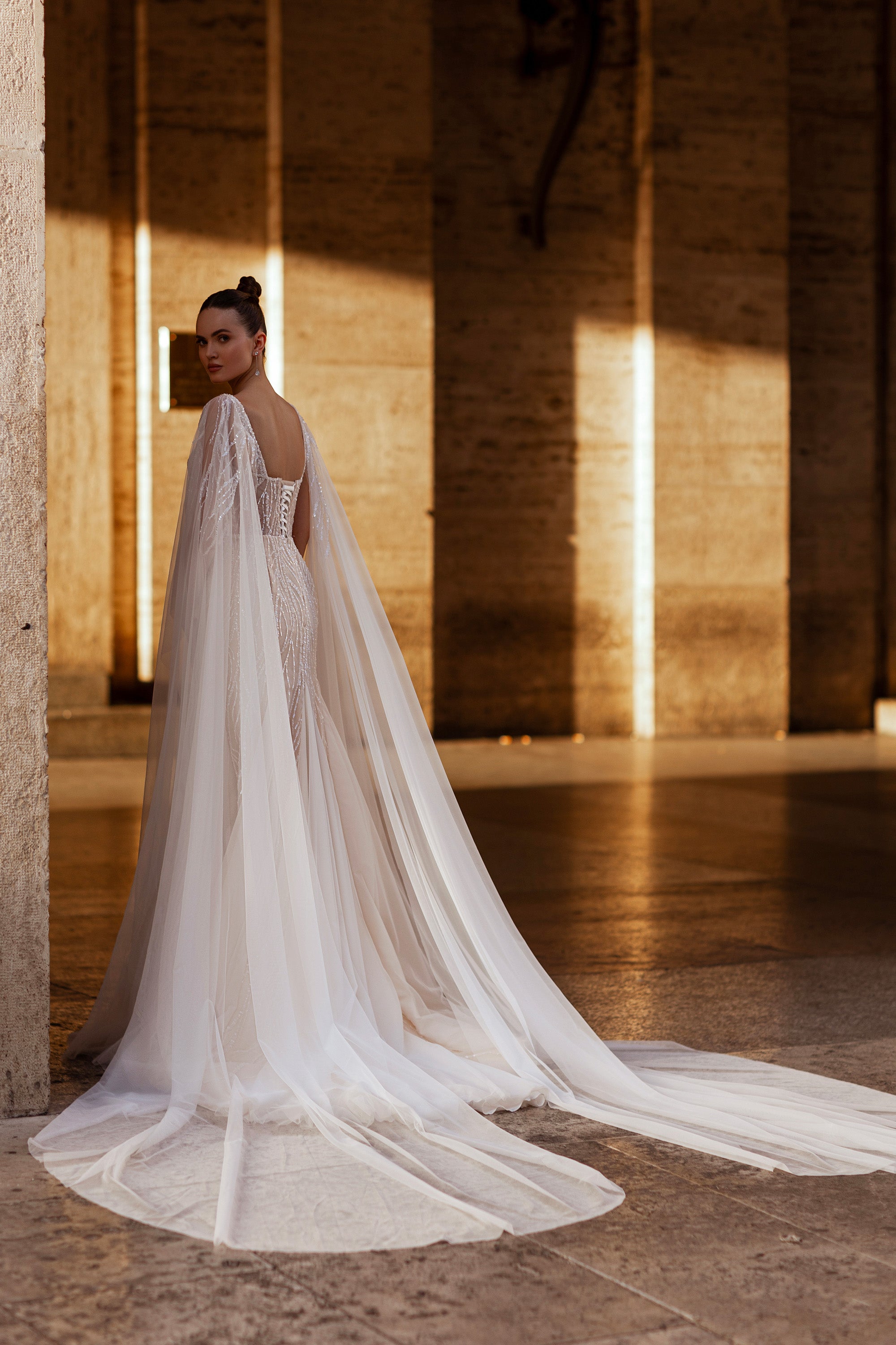 Ivory wedding dress with a beaded open back, long sheer cape, and flowing train