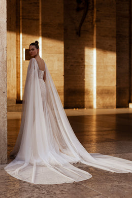 Ivory wedding dress with a beaded open back, long sheer cape, and flowing train