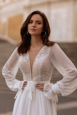 Ivory wedding dress with a deep V-neck beaded bodice, sheer long sleeves, and gathered flowing skirt