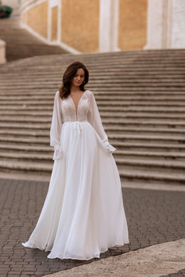 Full-length ivory wedding dress with a beaded V-neck bodice, sheer sleeves, and flowing A-line skirt