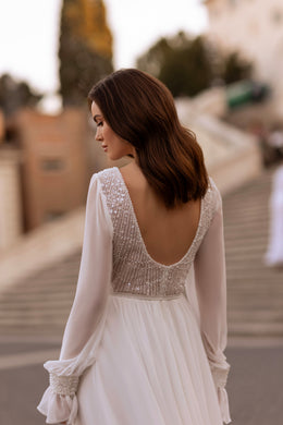 Low scoop-back ivory wedding dress with a beaded bodice, sheer long sleeves, and flowing skirt