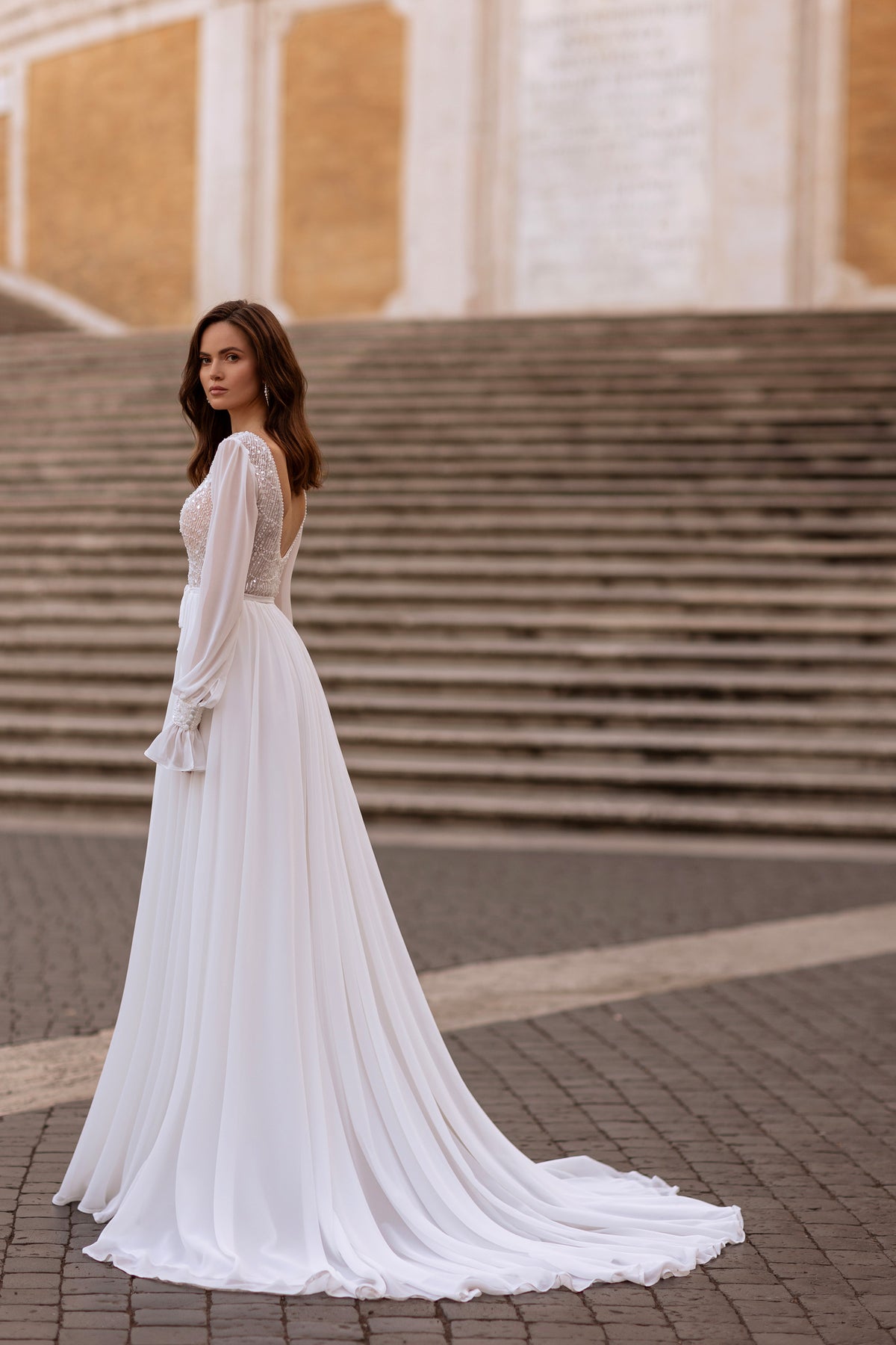Ivory A-line wedding dress with sheer sleeves, beaded bodice, and a long flowing train