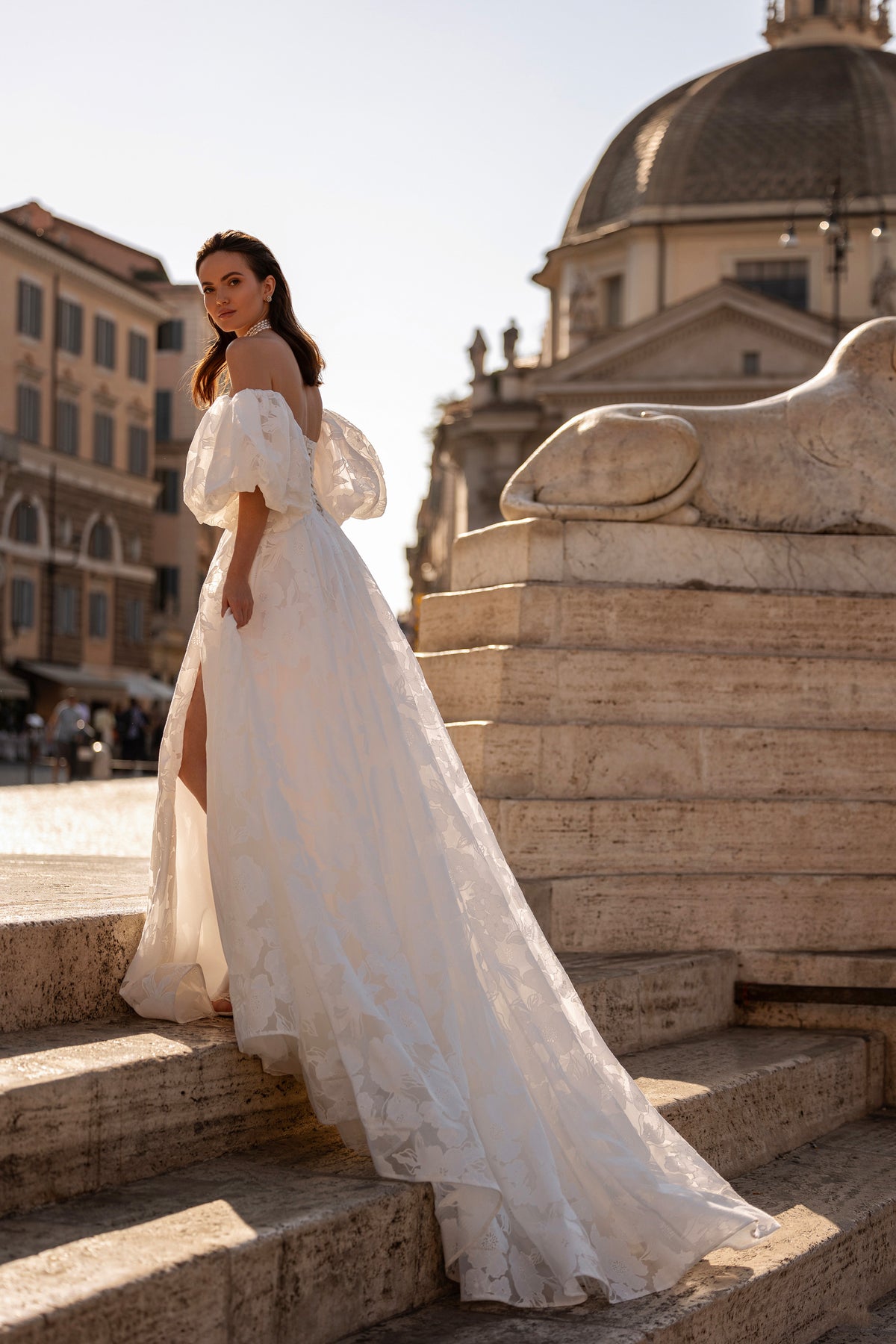 White A-line wedding dress with voluminous puff sleeves, floral texture, and a sweeping train