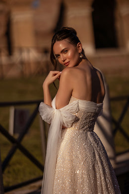 Close-up of the low open back, glittering beadwork, and sheer detachable sleeves on an ivory wedding dress