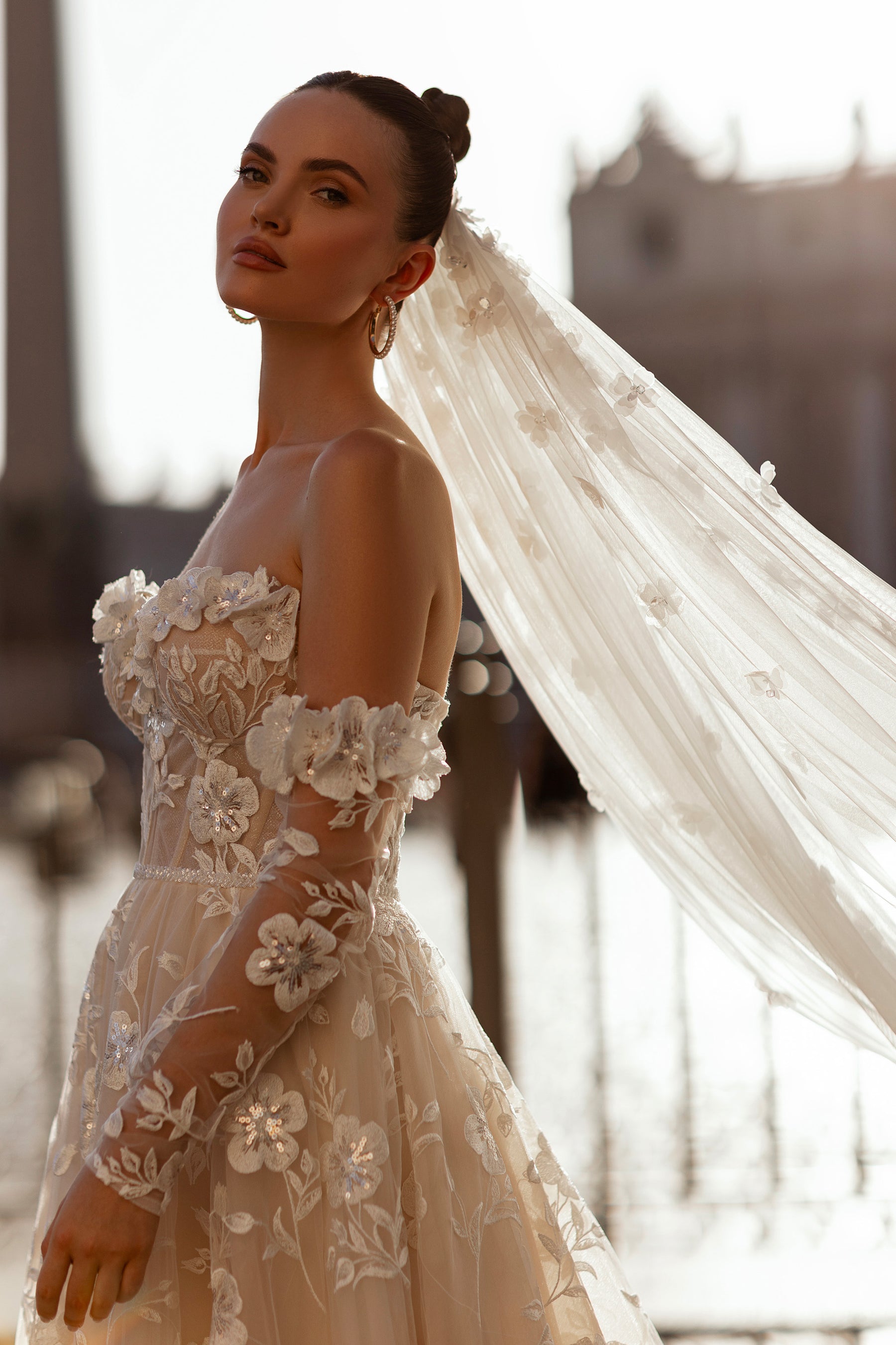 Side view of an ivory wedding dress with floral appliqués, sheer off-the-shoulder sleeves, and a fitted bodice