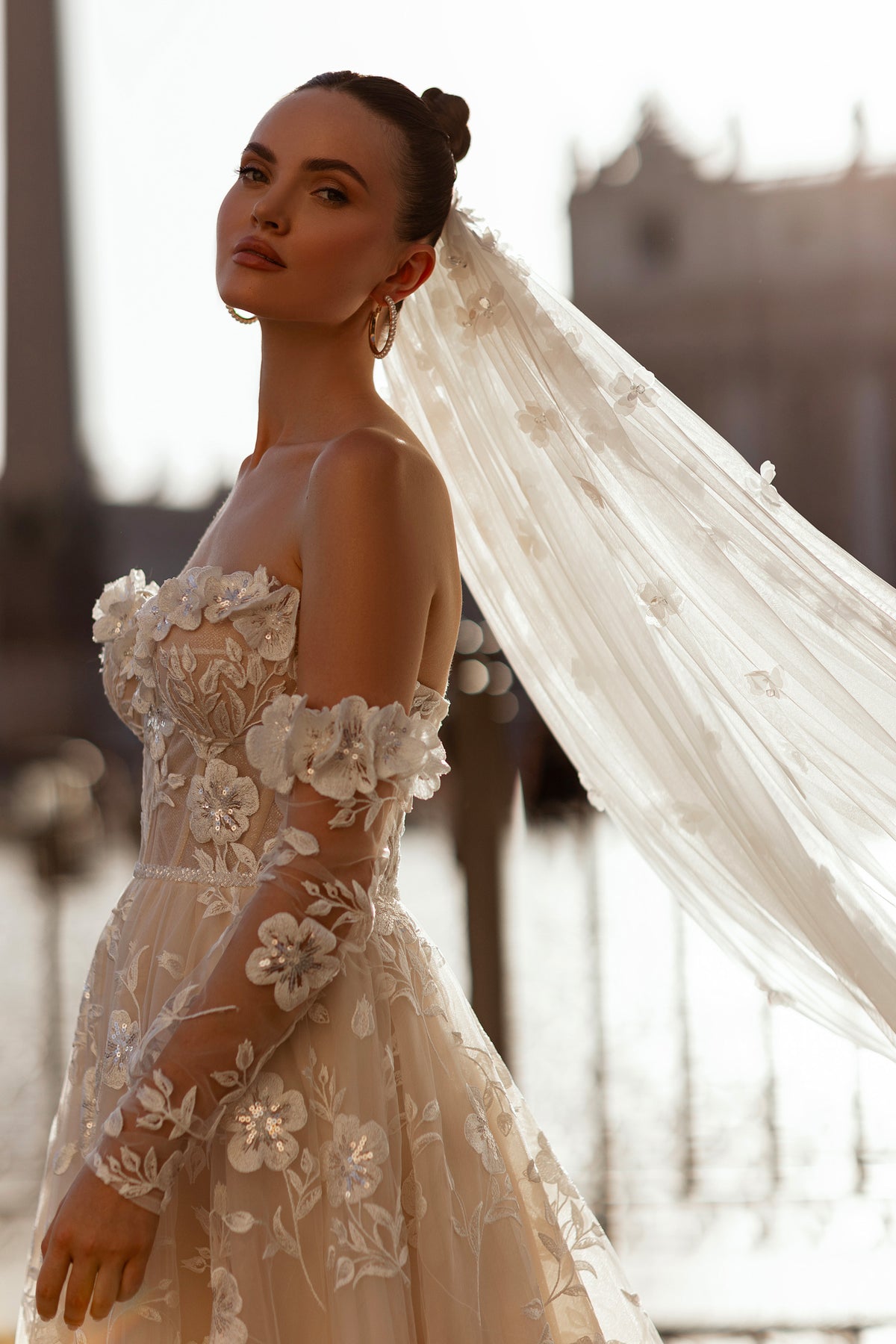 Side view of an ivory wedding dress with floral appliqués, sheer off-the-shoulder sleeves, and a fitted bodice