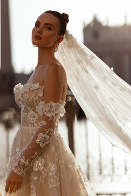 Side view of an ivory wedding dress with floral appliqués, sheer off-the-shoulder sleeves, and a fitted bodice
